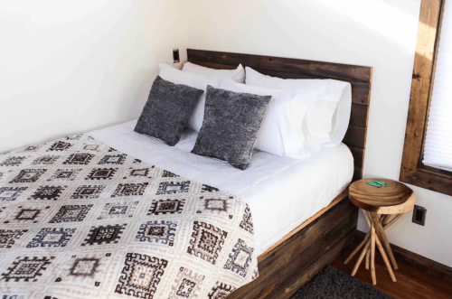 Cozy bedroom featuring a wooden bed, patterned blanket, two pillows, and a small side table.